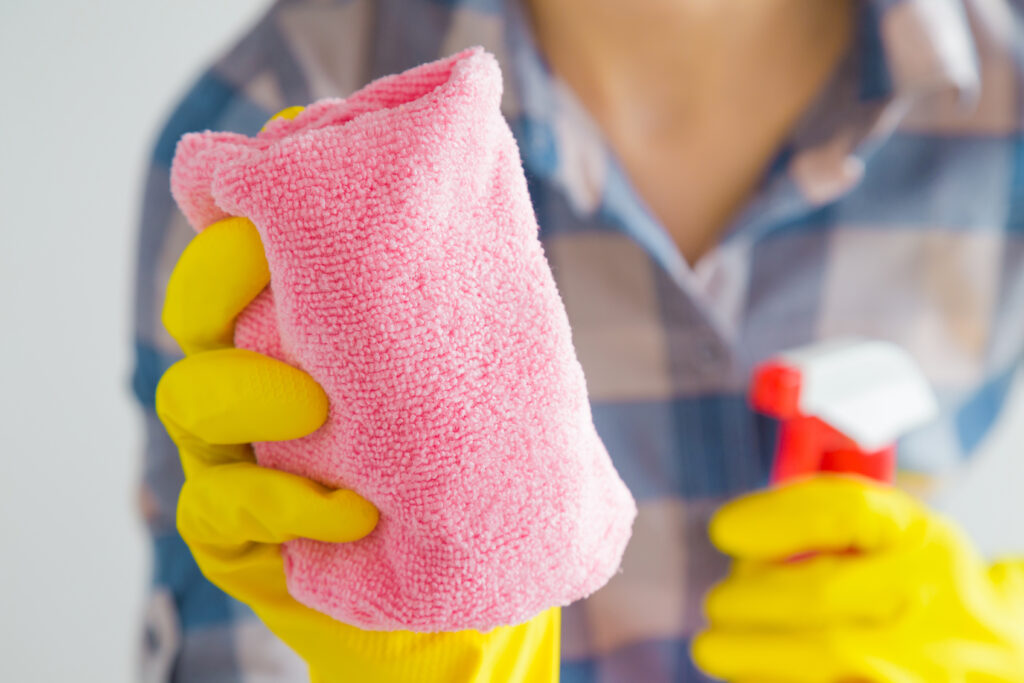 woman holds red microfiber cloth and spray bottle while wearing yellow cleaning gloves