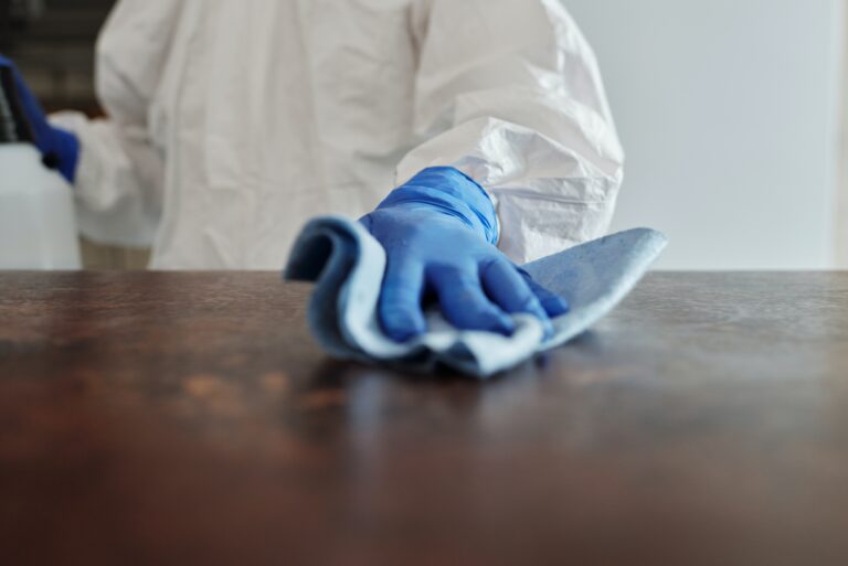 Person with blue medical gloves on and a protective outfit cleaning a wooden surface