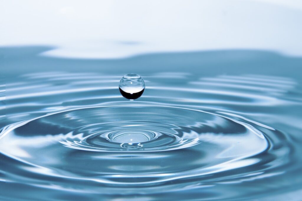 Closeup shot of a water droplet in a pool of water with a visible ripple on the water surface
