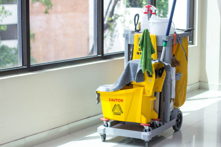 Custodian cleaning cart in a school hallway with dirty rags and a mop