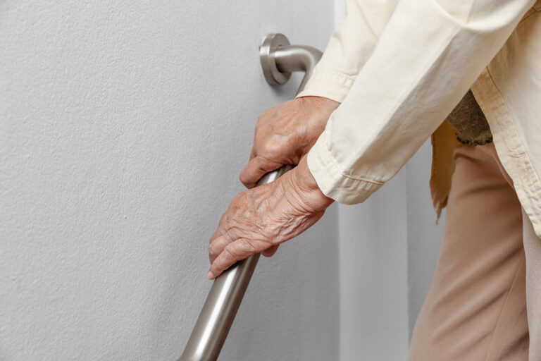 Elderly woman at a senior living facility holding a metal handrail while walking down steps