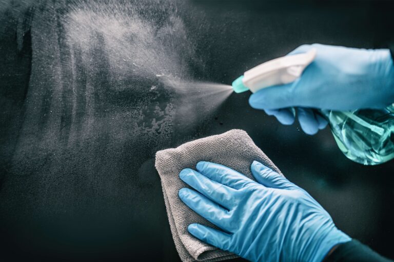 Person with rubber gloves on cleaning a surface with cleaning solution